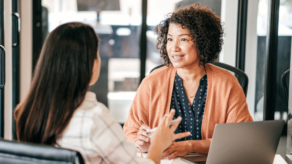 Mercado de Trabalho: O Que Esperar para o Segundo Semestre de 2025? 2 Mulheres em reunião de negócios ou mentoria, discutindo tendências e estratégias de carreira no futuro do trabalho.